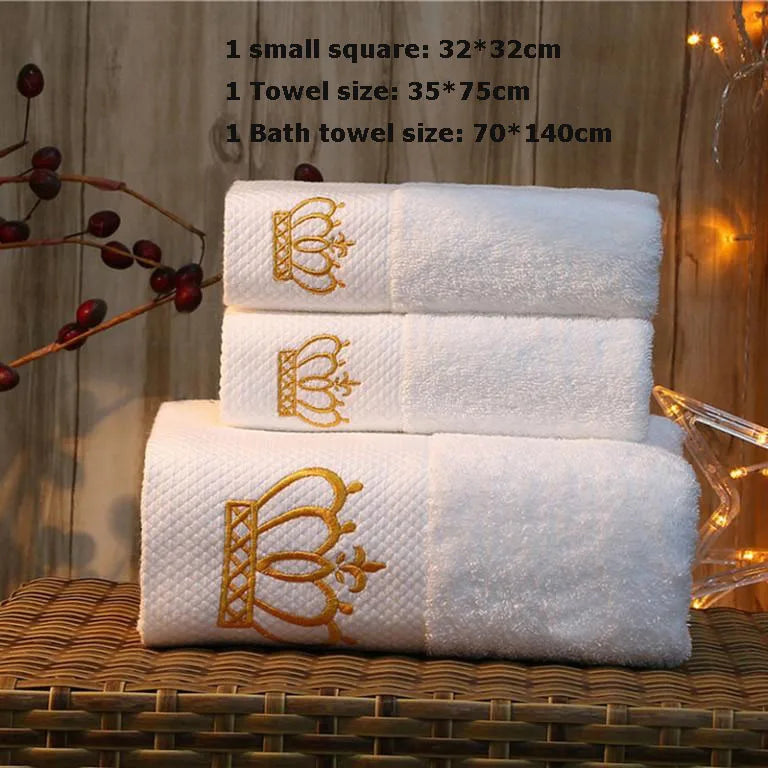 Set of white towels with gold embroidery on a wooden surface.