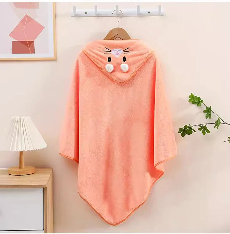 Coral-colored hooded blanket with cartoon face design on a hanger against a light wall.