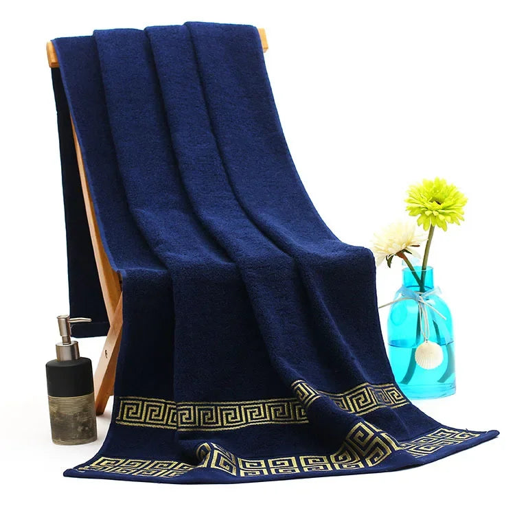 Navy blue towel with gold patterns draped over a chair, with a bottle and vase in the background.