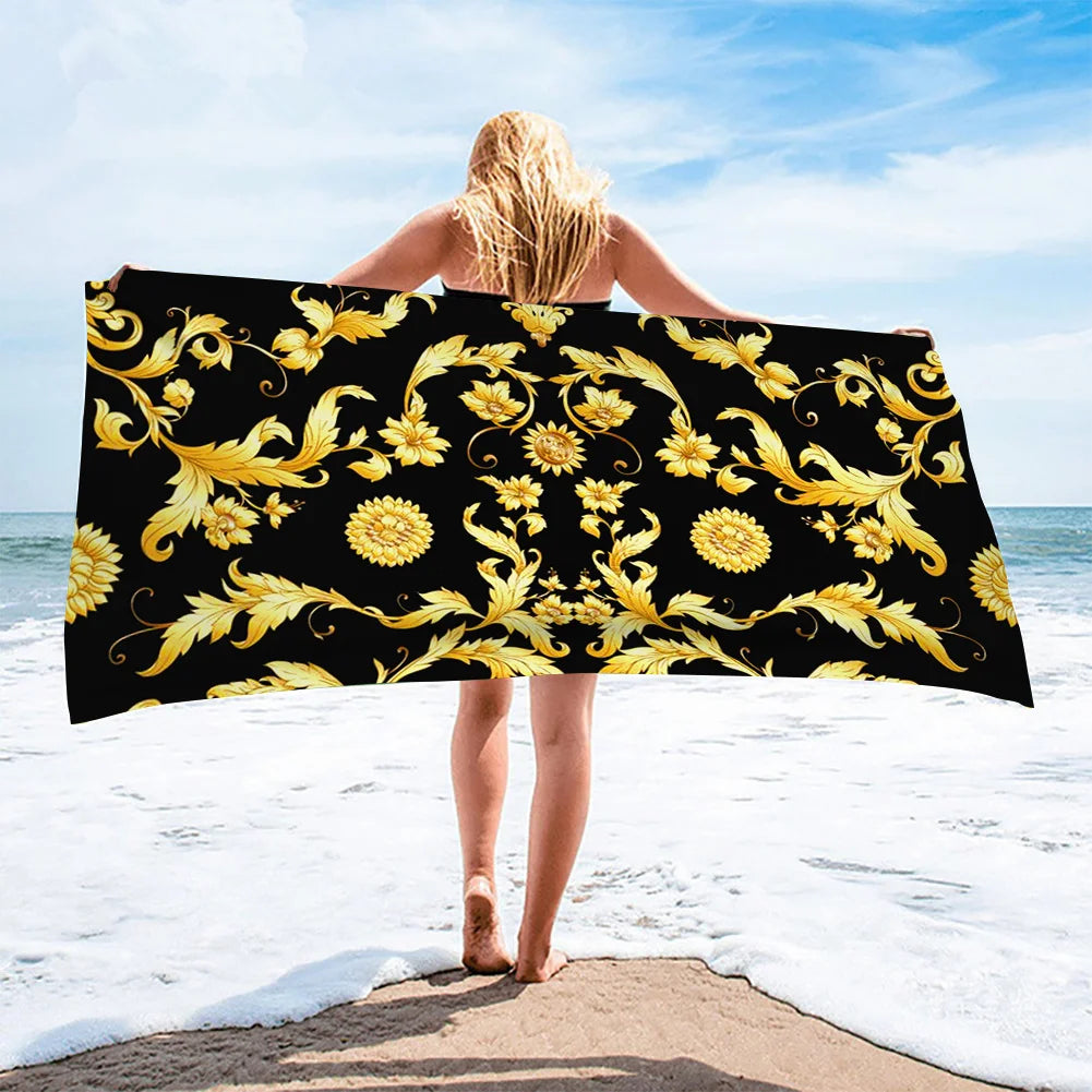 Person holding a large black beach towel with gold floral patterns on a beach.