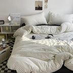 Striped bedding set on a bed in a bedroom with a mirror and books on a shelf.