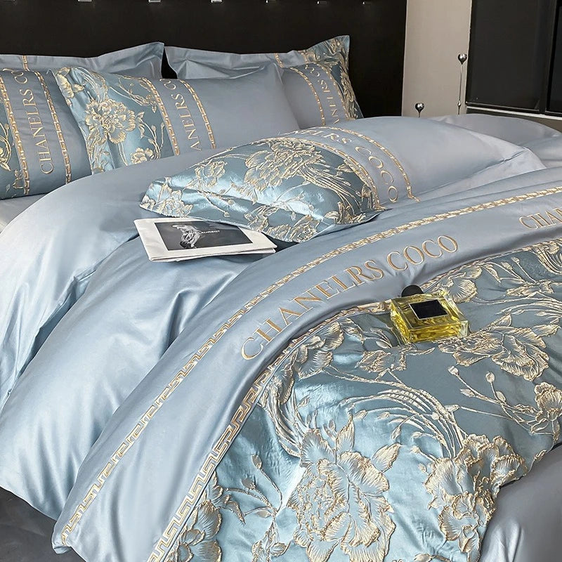 Luxury light blue bedding set with gold embroidery featuring 'Chanel's Coco' on a bed.