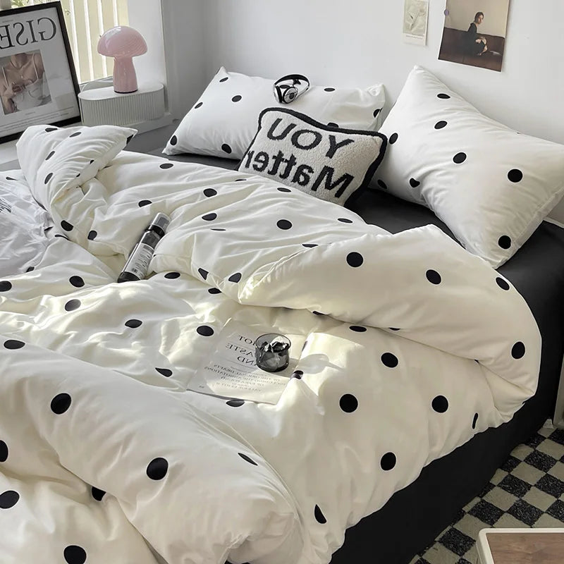 White polka dot bedding set on a bed with black and white pillows.