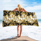 Person holding a decorative towel with gold patterns on a beach