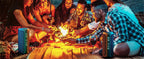 Group of friends gathered around a fire pit with sparklers, enjoying a casual outdoor gathering.