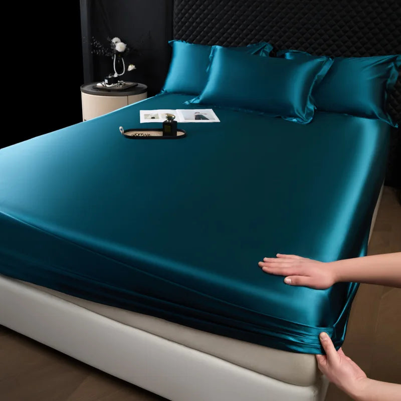 Teal satin sheet set being fitted onto a bed with a person's hands visible.
