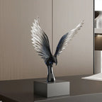 Decorative sculpture of a bird with outstretched wings on a pedestal against a neutral wall.