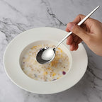 Hand holding a spoon over a bowl of cereal on a marble surface