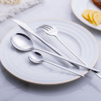 Silver cutlery set on a white plate with a gold rim, placed on a light gray surface.