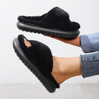 Black fuzzy slippers being worn on a light gray background