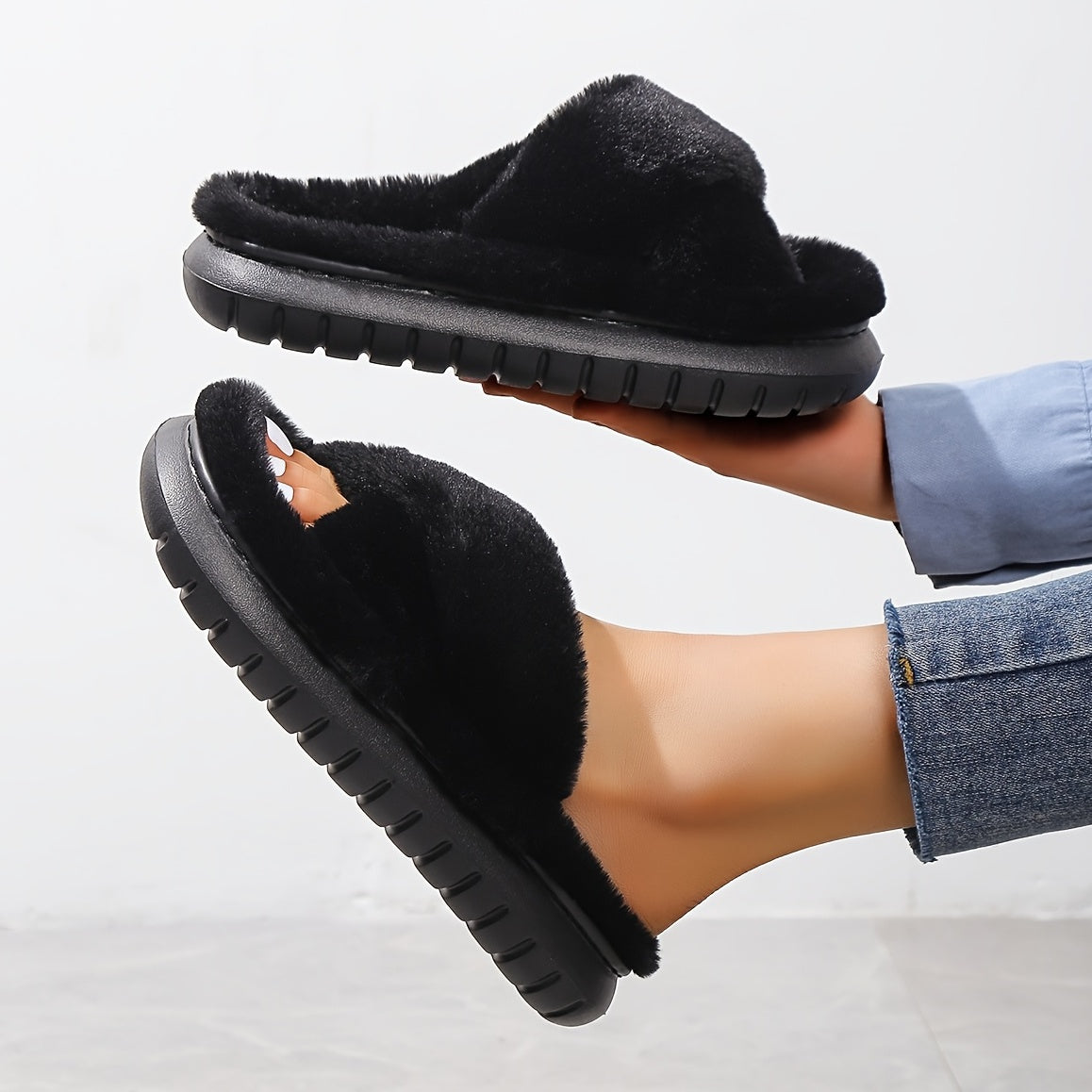 Black fuzzy slippers being worn on a light gray background