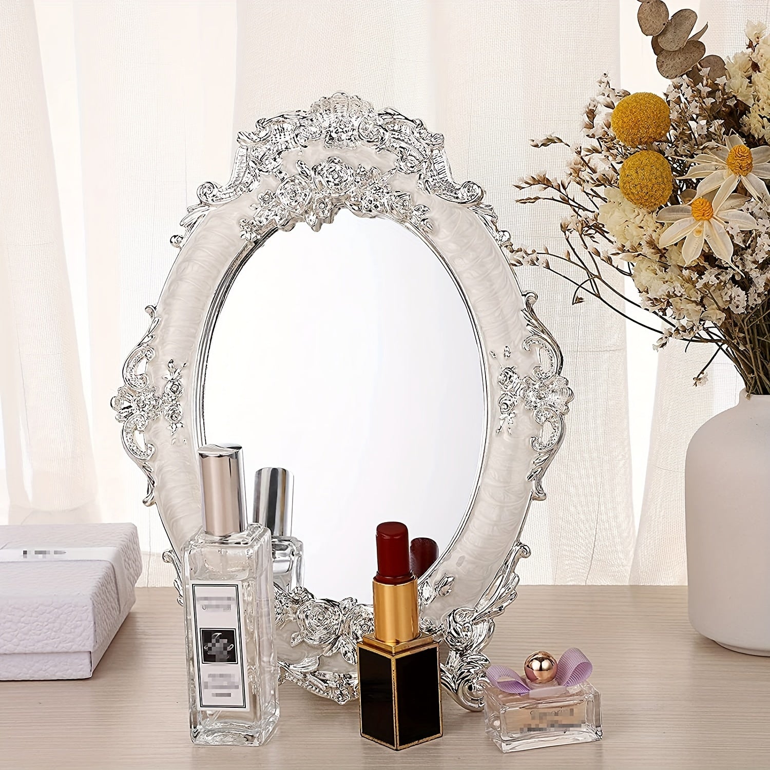 Decorative mirror with floral frame on a table with beauty products and flowers.