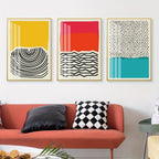 Three abstract art prints on a wall above a red sofa with decorative pillows.
