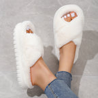 White fluffy slippers worn with denim jeans on a gray floor.