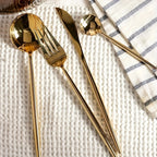 Gold cutlery set on a textured white surface with a striped cloth.