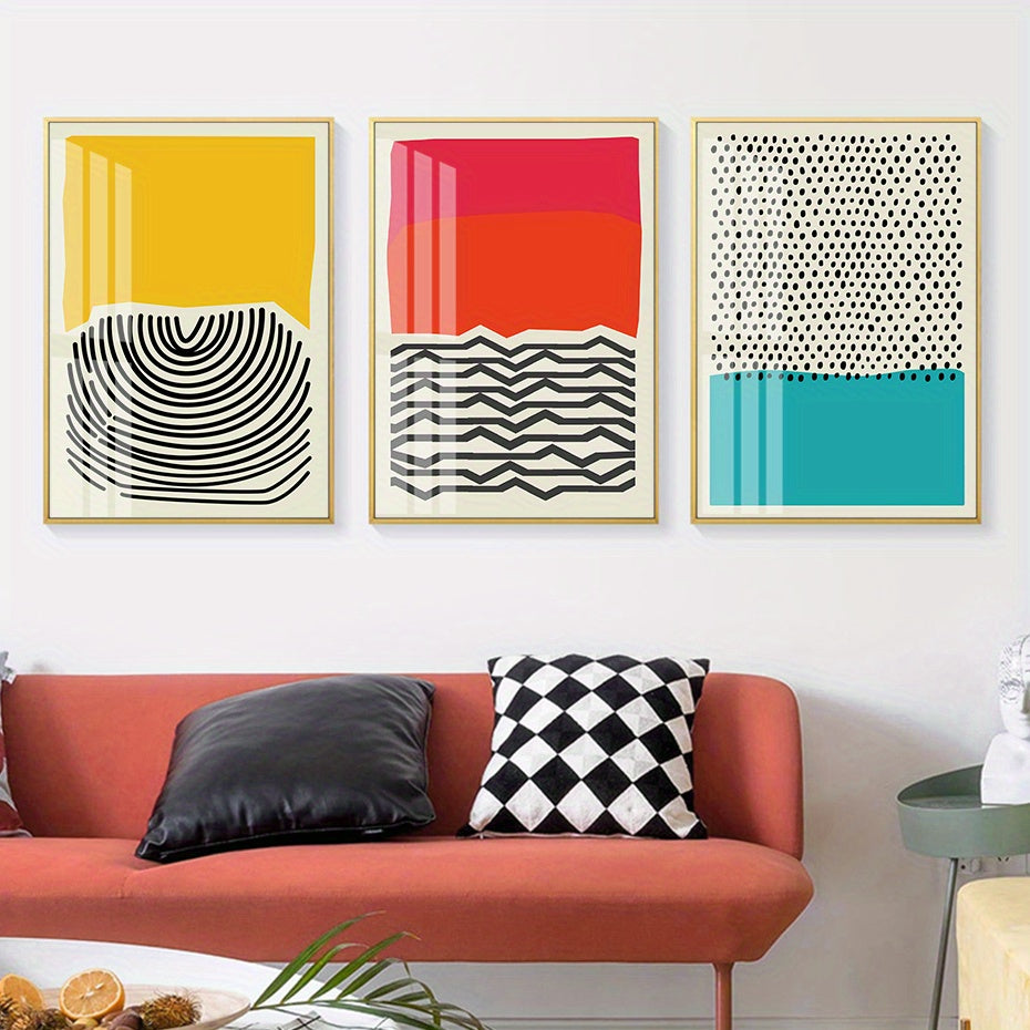Three abstract art prints on a wall above a red sofa with decorative pillows.