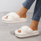 White fluffy slippers worn with blue jeans on a light gray floor.