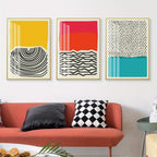 Three abstract art prints on a wall above a red sofa with decorative pillows.